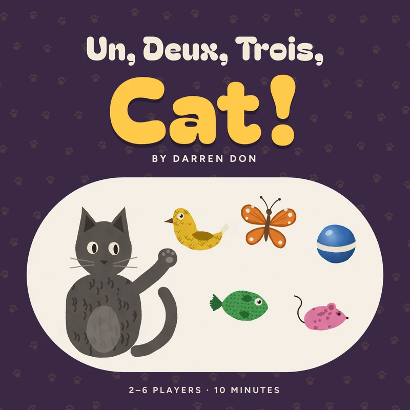 The box lid: Un, Deux, Trois, Cat! by Darren Don, with a painted grey cat reaching a paw toward the bird, butterfly, ball, fish and mouse on a cream rug, over plum with gold paw prints.