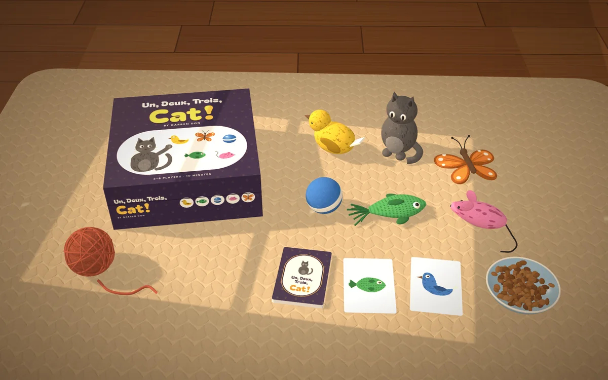 Un, Deux, Trois, Cat! mockup on a knit blanket in a sunbeam: the box, the felt toys, the deck and two cards, a ball of yarn and a bowl of kibble.